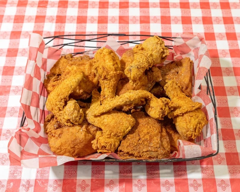 A wire basket filled with crispy fried chicken pieces on a red and white checkered tablecloth.