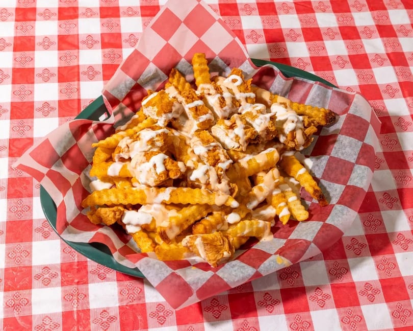 Crinkle-cut fries topped with crispy chicken pieces and drizzled with white and orange sauces.