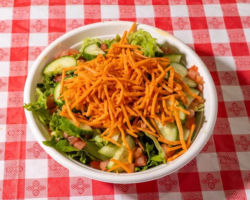 Fresh garden salad with lettuce, cucumbers, tomatoes, and shredded carrots on a red and white checkered tablecloth.