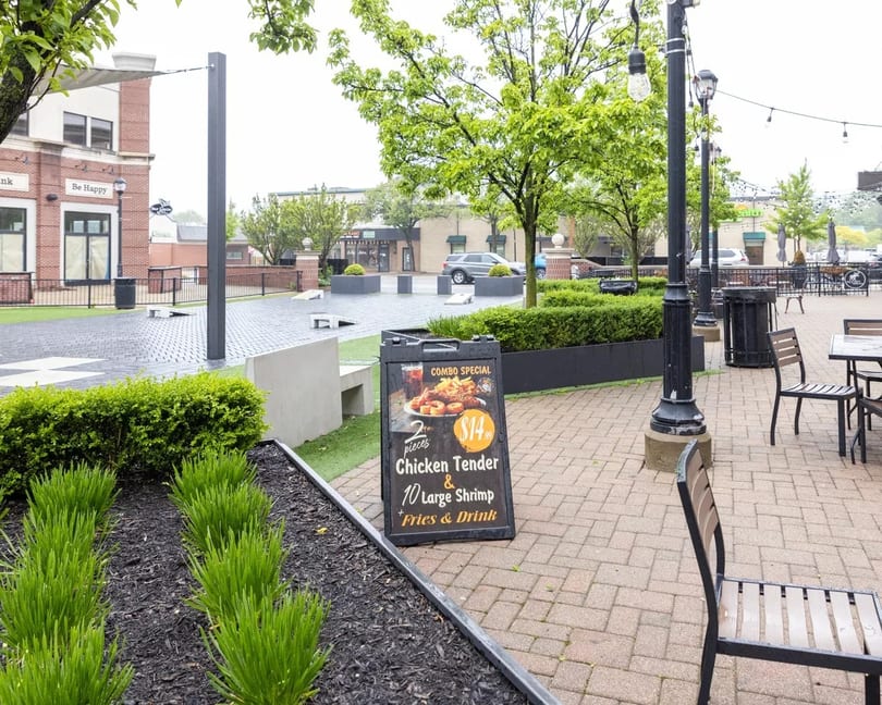 A restaurant combo special sign for chicken tenders and shrimp on a brick patio with outdoor seating.