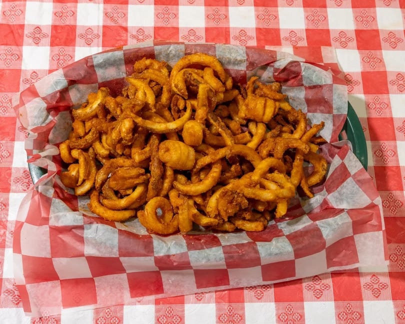 A basket of golden curly fries with seasoning, served on a red and white checkered tablecloth.