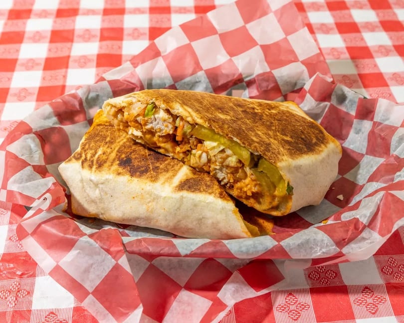 A grilled burrito, cut in half, revealing its filling, served in red and white checkered paper.
