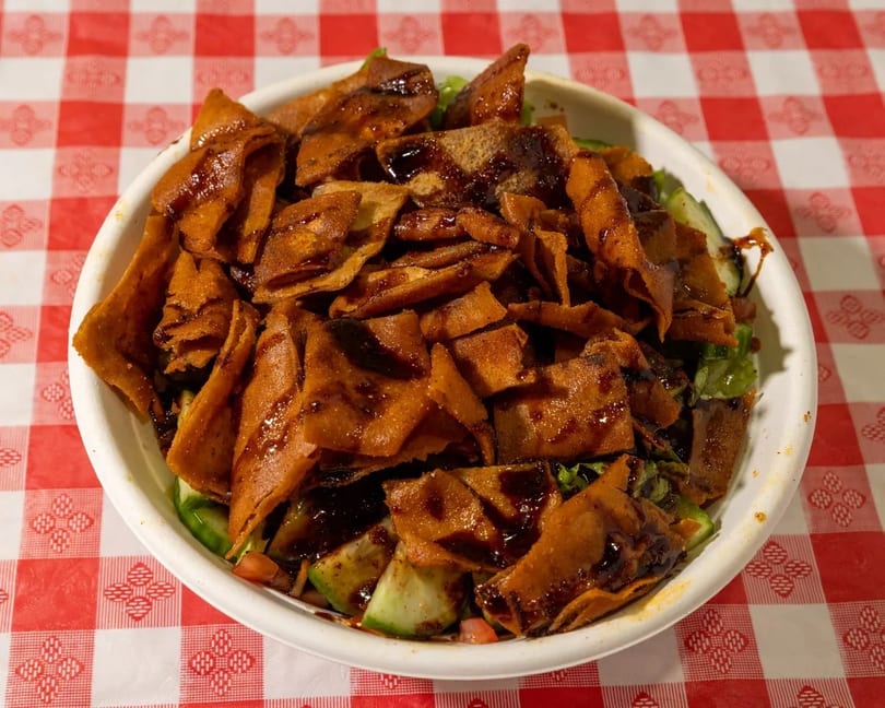 Fattoush salad with crispy pita bread, fresh vegetables, and a dark dressing on a red and white checkered tablecloth.