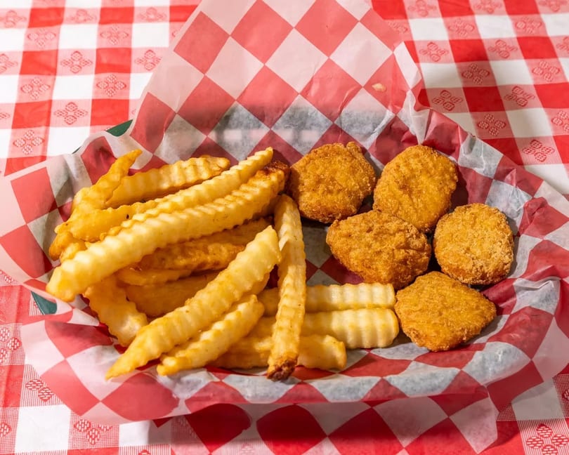 Basket of golden-brown crinkle-cut fries and chicken nuggets on a red and white checkered tablecloth.